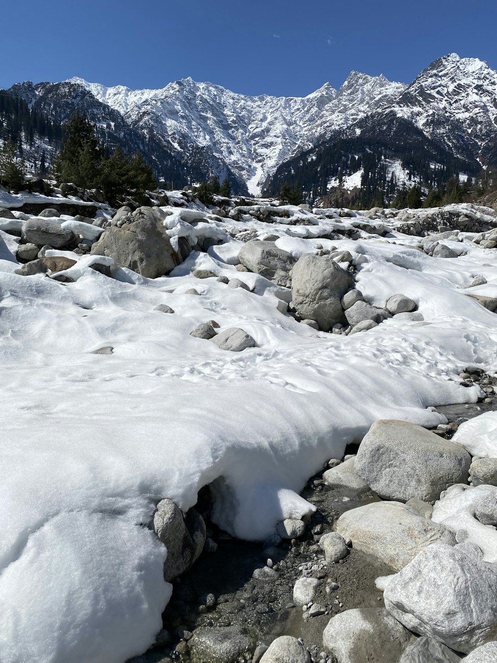 a rocky area with snow and mountains in the background