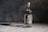 A bottle of Wild Common Tequila Blanco stands upright on a surface against a dark, textured background. The label indicates it is made from 100% agave, specifically Blue Weber agave.