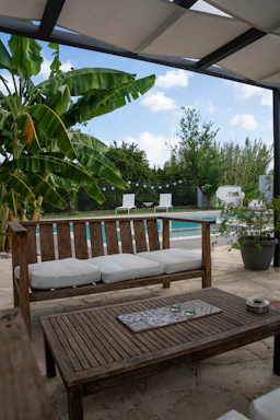 A cozy outdoor patio scene featuring a wicker pool lounger beside a wooden raised planter filled with vibrant flowers.