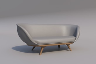 A modern, minimalist sofa with a grey upholstery and wooden legs. The smooth curves and sleek design give it a contemporary feel, while the slightly curved backrest and cushioned seat add comfort. The light background enhances the elegant simplicity of the furniture piece.