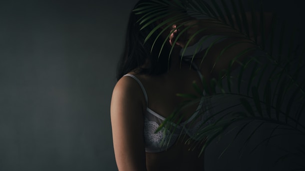 A softly lit boudoir scene with a model draped in delicate swimwear, surrounded by shadows and warm nude tones.