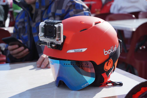 An action camera attached to a helmet, capturing a first-person view of a snowy mountain ski run.