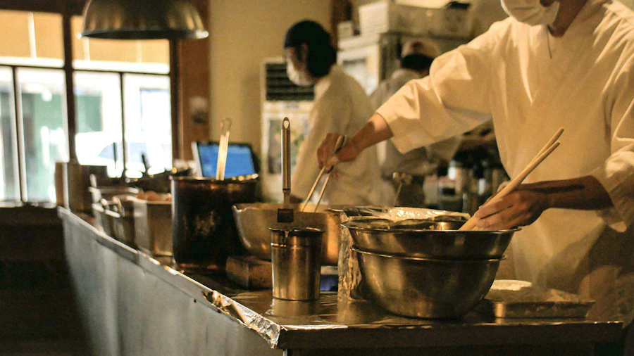 A chef in whites stirring a pot at the stove in a warm-lit kitchen