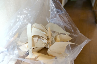 A pile of torn, beige material, possibly plaster or drywall, is inside a transparent plastic bag. The contents are spread out unevenly and the bag is open, revealing the texture and various sizes of the pieces.