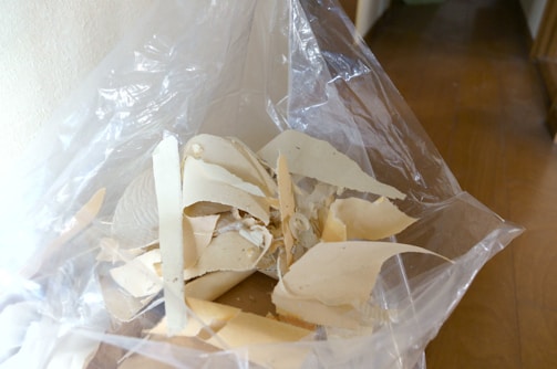 A pile of torn, beige material, possibly plaster or drywall, is inside a transparent plastic bag. The contents are spread out unevenly and the bag is open, revealing the texture and various sizes of the pieces.