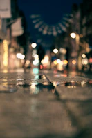 An urban street scene at dusk with colorful lights reflecting on wet pavement.
