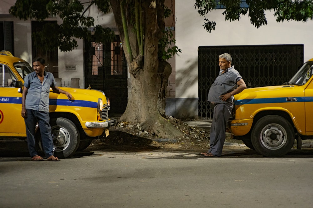 a couple of men standing next to a tree and a yellow car