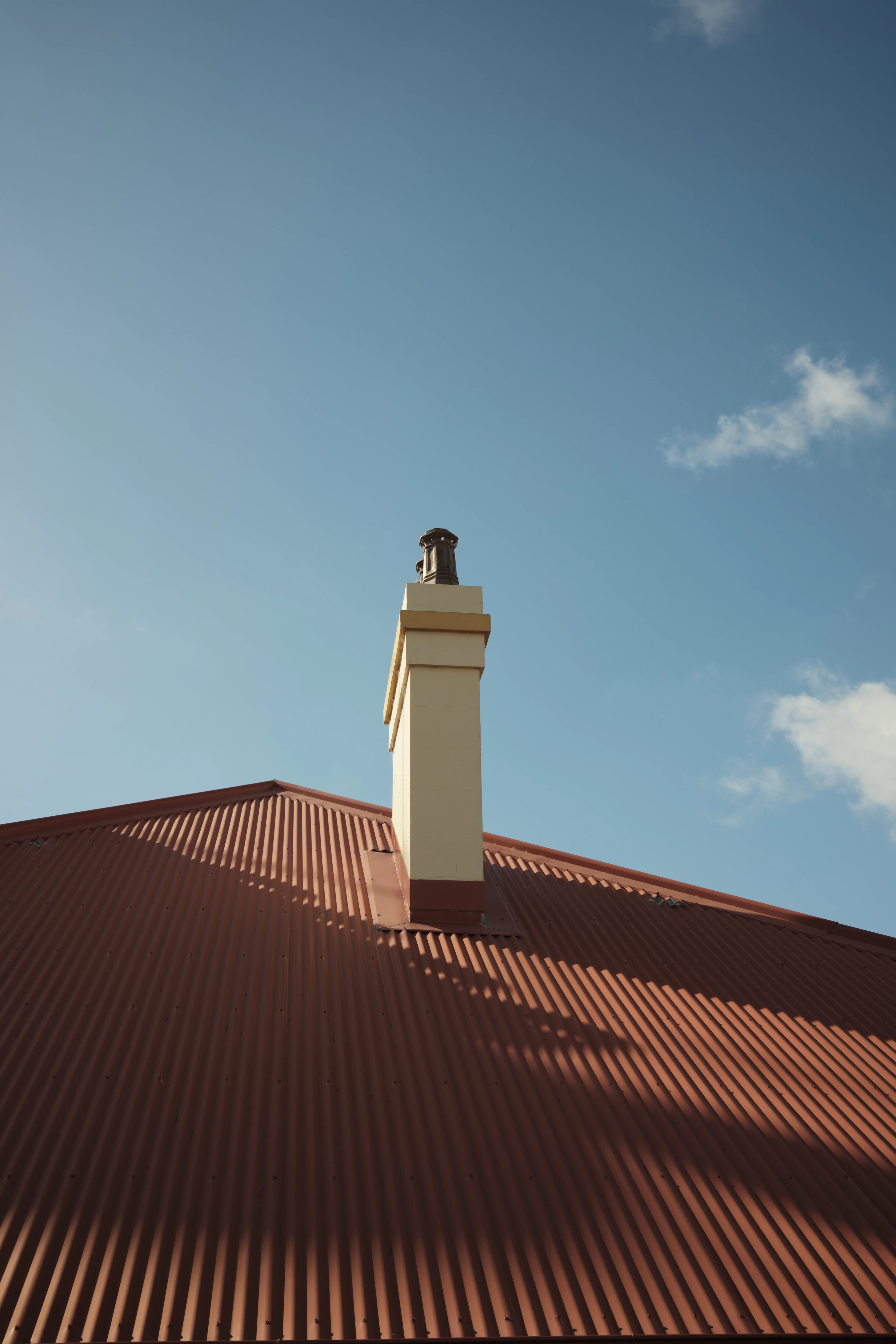 Chimney rising from a red corrugated roof beneath a pale blue sky