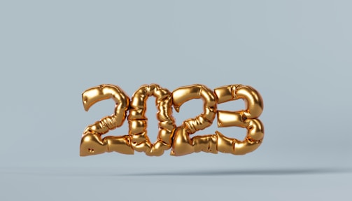 Golden balloon numbers form the year 2023 against a light blue background, creating a festive and celebratory atmosphere. The metallic sheen of the balloons adds a sense of elegance and festivity.