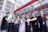 A group of seven people wearing black shirts and green face masks are standing outside a store with a sign that reads 'Tops Market.' They are holding up smartphones displaying the same green logo.