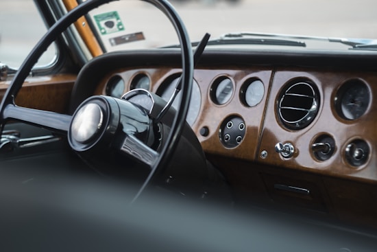 A vintage car dashboard with a classic wooden finish. The dashboard features round gauges, a steering wheel with a simple, retro design, and metal accents. The atmosphere suggests the elegance and style of an older model car.