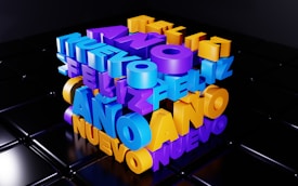 Colorful 3D text spells out the phrase 'Feliz A&ntilde;o Nuevo' in vibrant colors including purple, blue, and yellow. The letters are stacked in a cube arrangement on a glossy black surface, giving a festive and modern look.