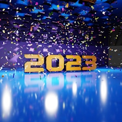 Large golden numbers displaying '2023' are positioned against a vibrant backdrop with a reflective blue floor. Multicolored confetti is suspended in the air, adding a festive and celebratory atmosphere. The background is a deep blue and purple, enhanced with lighting effects that give a party ambiance.