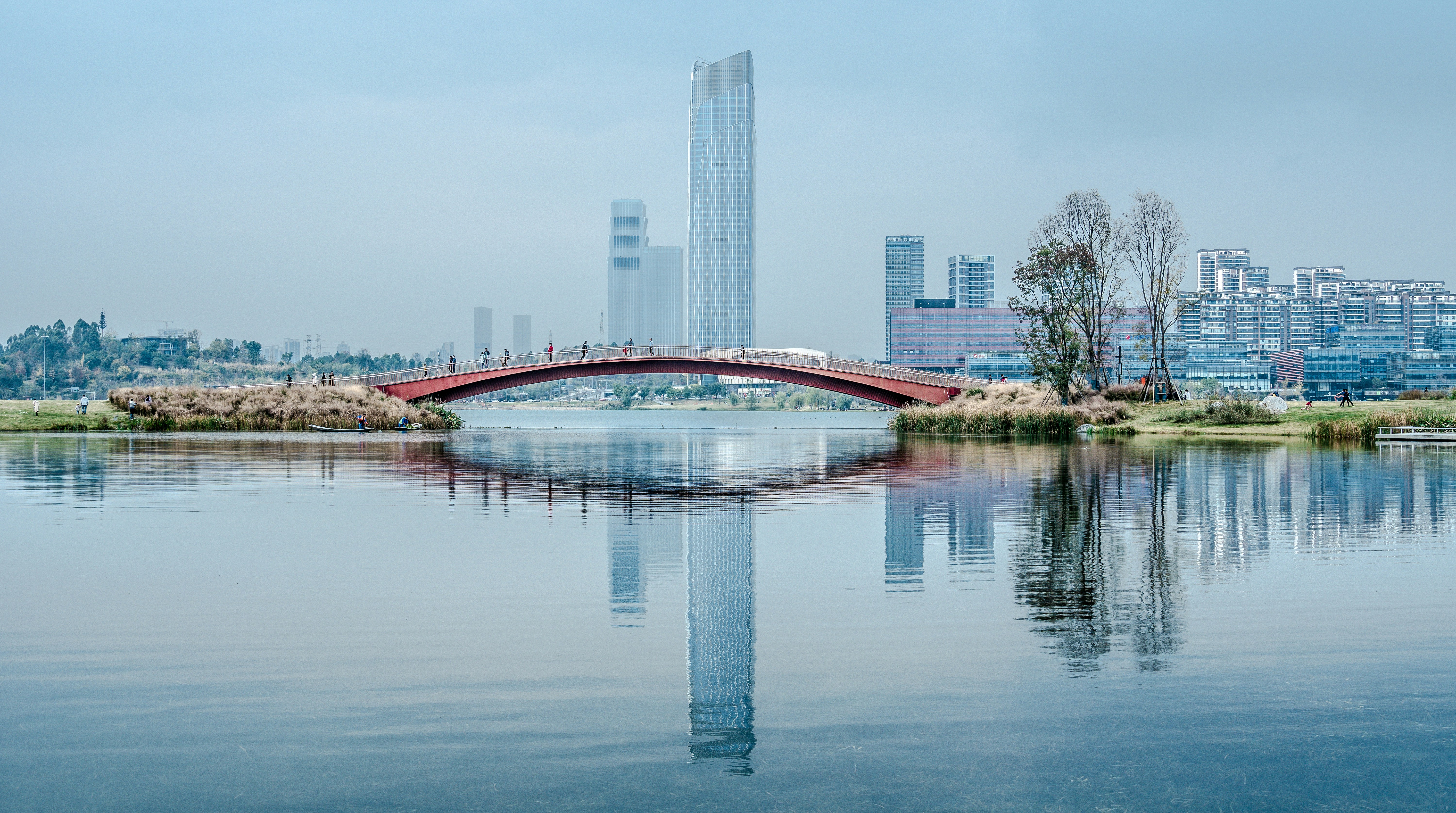 Panoramic daytime view of a bridge crossing the water with the city of Chengdu in the background