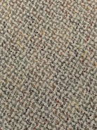 A close-up view of a textured carpet with a speckled pattern. The surface consists of tightly woven loops in various colors, predominantly gray, with interspersed specks of red, orange, yellow, and green.