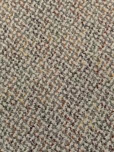 A close-up view of a textured carpet with a speckled pattern. The surface consists of tightly woven loops in various colors, predominantly gray, with interspersed specks of red, orange, yellow, and green.