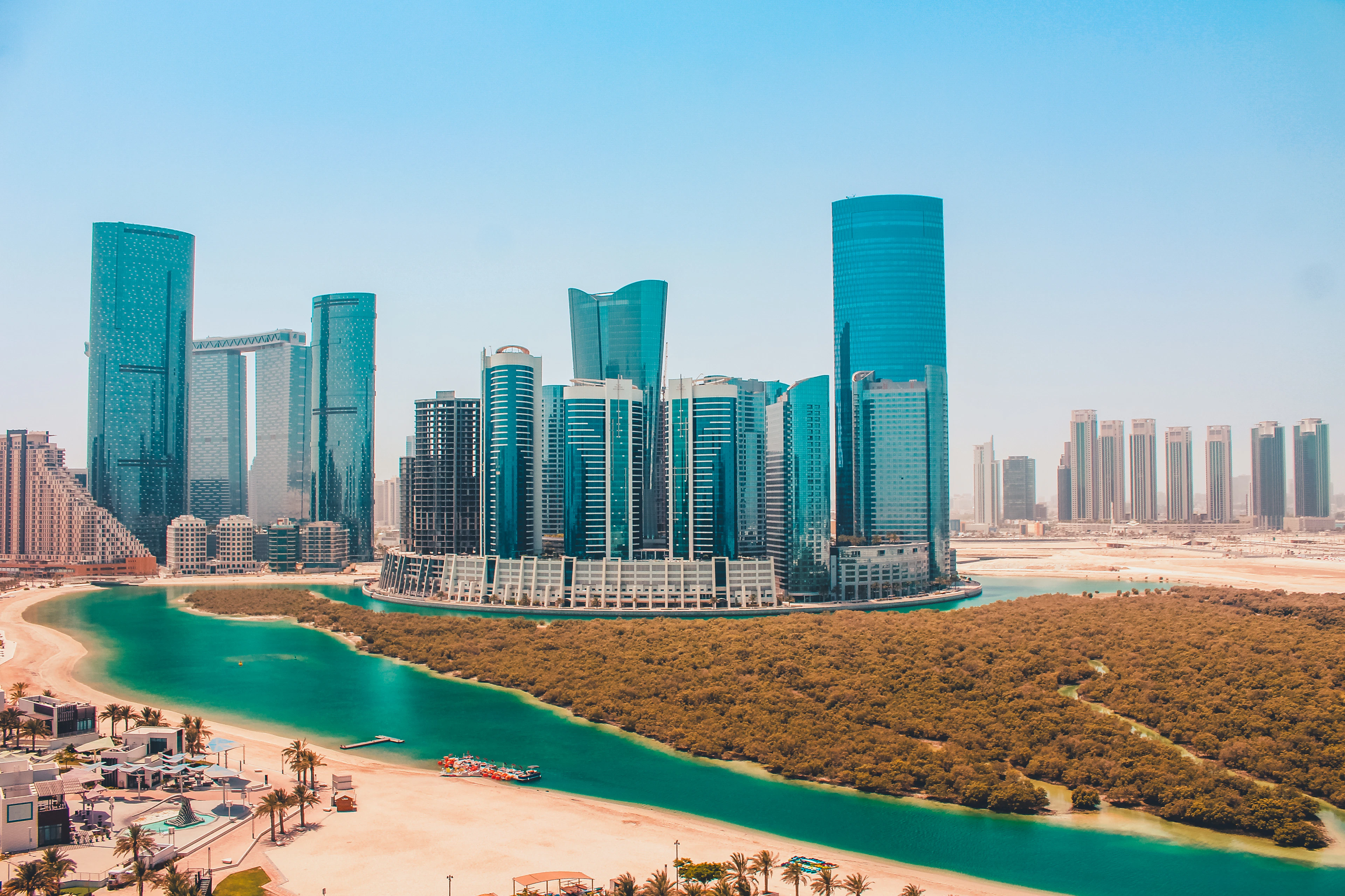Abu Dhabi's glass towers rise beside a turquoise mangrove canal and green shoreline.