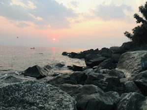 Sunset view over calm sea with a small boat anchored near a secluded beach.