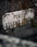 An aged, weathered stone sign with the words 'PORTO EUGENIO VERALLI' is set against a rough stone wall. Moss and small plants are growing around the edges of the sign, adding a natural and rustic feel.