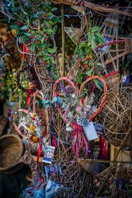 A decorative display featuring wicker crafts with intricate patterns adorned with greenery and red berries. Some of the wicker pieces are shaped like hearts, embellished with dried flowers and colorful ribbons. Price tags can be seen attached to several items.