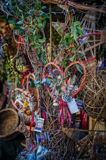 A decorative display featuring wicker crafts with intricate patterns adorned with greenery and red berries. Some of the wicker pieces are shaped like hearts, embellished with dried flowers and colorful ribbons. Price tags can be seen attached to several items.