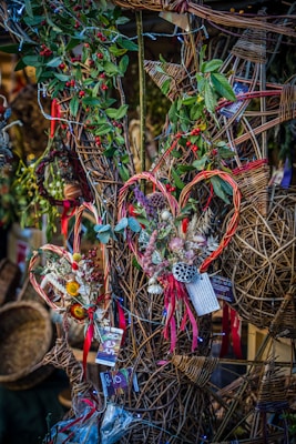 A decorative display featuring wicker crafts with intricate patterns adorned with greenery and red berries. Some of the wicker pieces are shaped like hearts, embellished with dried flowers and colorful ribbons. Price tags can be seen attached to several items.