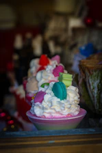 Close-up of luxurious dessert shots in glass cups with creamy layers and decorative toppings, set on a soft pink background.