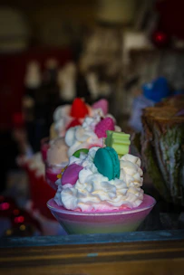 Close-up of luxurious dessert shots in glass cups with creamy layers and decorative toppings, set on a soft pink background.