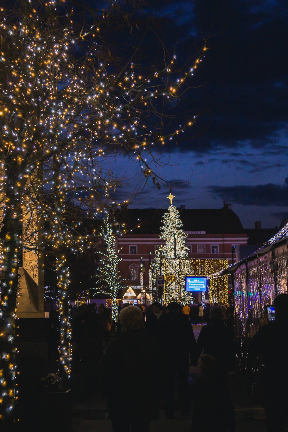 a group of people standing in front of a building with christmas lights