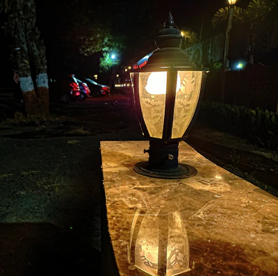 Close-up of a sleek navy outdoor lantern casting warm light on a sandy stone pathway.