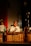 A man in traditional attire plays a wooden xylophone-like musical instrument. He is seated in front of a music stand holding sheets. The scene is dimly lit, creating a focused spotlight on the musician, enhancing the cultural and performance ambiance.