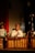 A man in traditional attire plays a wooden xylophone-like musical instrument. He is seated in front of a music stand holding sheets. The scene is dimly lit, creating a focused spotlight on the musician, enhancing the cultural and performance ambiance.