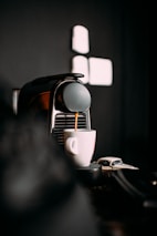 A sleek espresso machine dispensing coffee into a white cup. The background is dark, creating a stark contrast that highlights the coffee-making process.