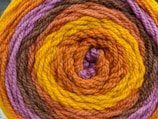 A close-up view of a rolled-up skein of yarn featuring concentric rings of different colors. The yarn is tightly wound, showcasing a vibrant pattern with distinct layers of color.