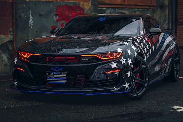 An elegant convertible with a classic American flag design parked near a battlefield historic marker.