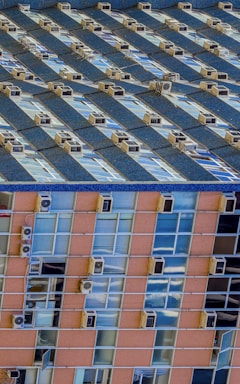 A vertical image showcasing two different building facades. The upper section of the image features rows of windows and air conditioning units on a blue building. The lower section depicts a different building with rows of windows and air conditioning units on an orange and glass facade.