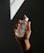 A hand holding a clear bottle labeled 'Pure Solution Essence,' with a minimalistic design. The background is dark with a geometric light pattern projected onto it.