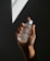 A hand holding a clear bottle labeled 'Pure Solution Essence,' with a minimalistic design. The background is dark with a geometric light pattern projected onto it.
