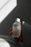 A serene close-up of a hand holding a small bottle of 薑薑好滴錠 with soft natural light and herbal leaves in the background.