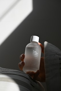 A hand gently holds a frosted glass bottle labeled 'Pure Solution Essence' against a soft, diffused light background, creating a serene and tranquil atmosphere.
