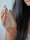 A hand with natural nails gently holds a frosted glass bottle labeled 'Pure Solution Essence' against a backdrop of long, dark hair. The focus is on the elegant bottle and the soft texture of the hair.