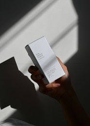 A hand holds a white box labeled 'Pure Solution Essence' against a backdrop with dramatic shadows. The box features minimal design with text in English and another language.