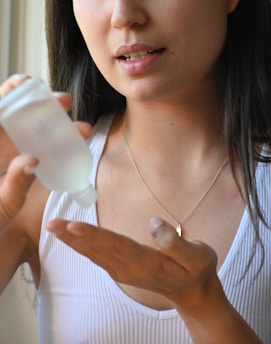 A close-up of a woman gently spraying a transparent hair growth product onto her scalp.