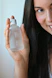 A close-up of a smiling woman with glowing skin holding a Luminara skincare bottle in a sunlit room.