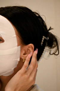 A close-up of a woman gently applying a hydrating Korean face mask, her skin glowing softly in natural light.