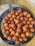 A collection of round, golden-brown fried dough balls arranged on a wire mesh tray set inside a round, metal container. The texture appears crispy and they are likely freshly cooked, glistening with a bit of oil.