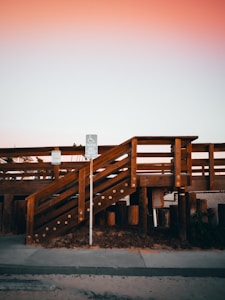 A wooden ramp structure leads up from a sidewalk, accompanied by a wheelchair-accessible parking sign. The warm hues of an evening sky cast a serene atmosphere over the scene.