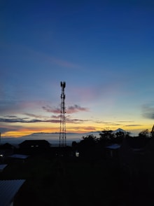 A construction worker inspecting a tall communication tower at sunset.