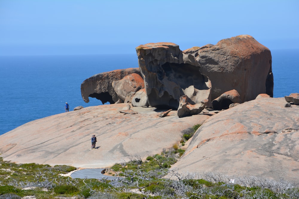 people walking on a path between large rocks on a cliff