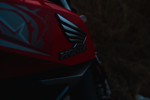 A close-up view of a red motorcycle with the Honda logo prominently displayed. The design includes sleek, angular lines and hints of a graphic pattern on the bodywork.